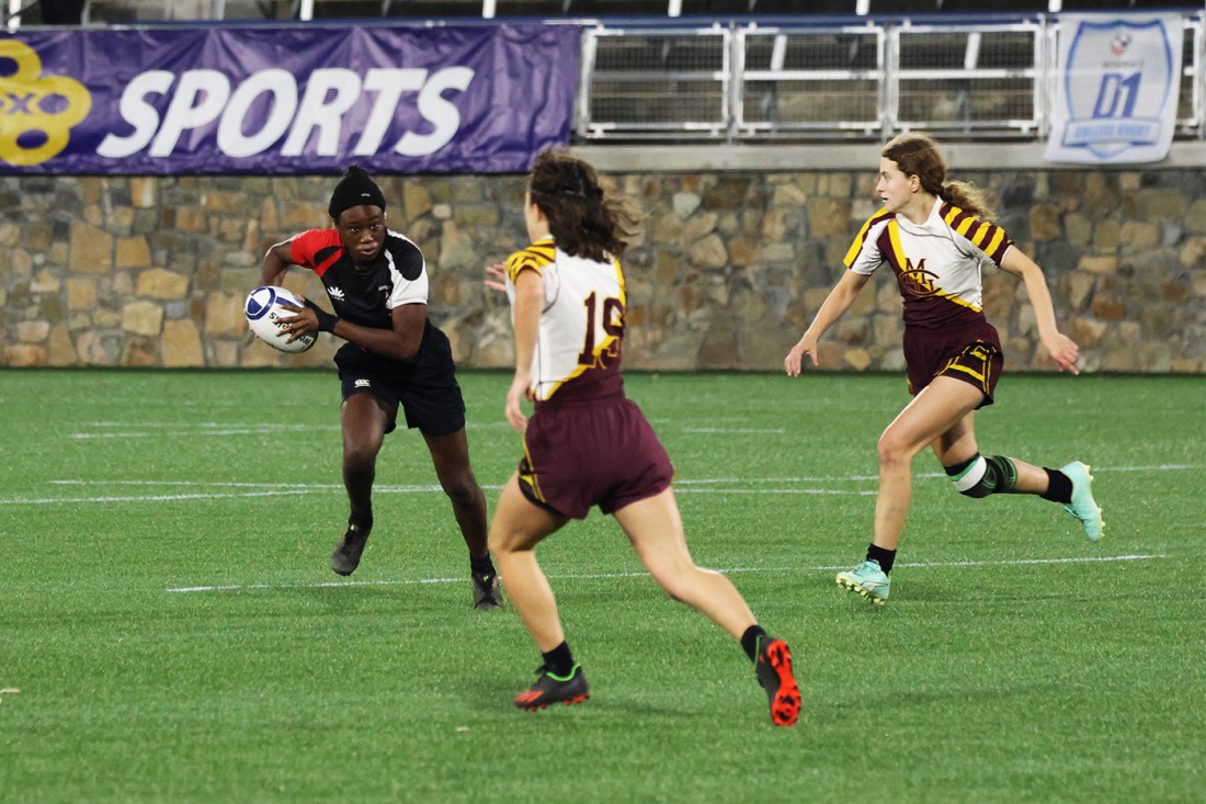 Northeastern womens rugby player running towards opponents with the ball. 