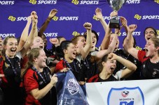 Northeastern womens rugby team cheering and holding a trophy.