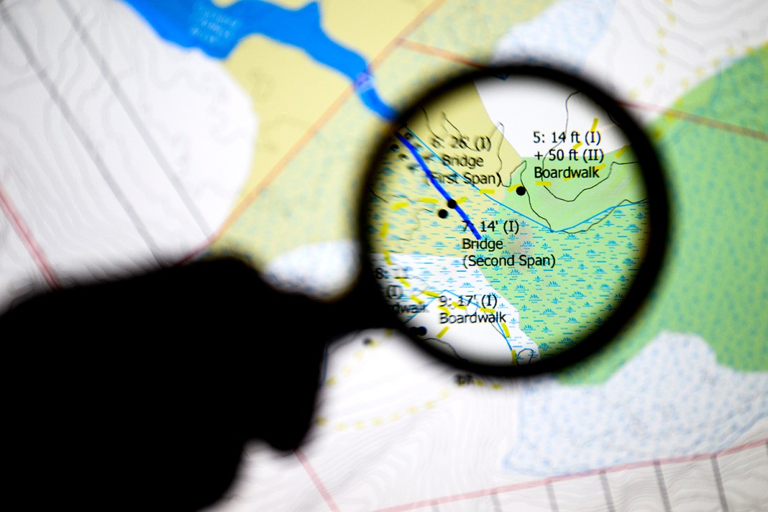 Silhouette of a magnifying glass hovering over a map of Maine