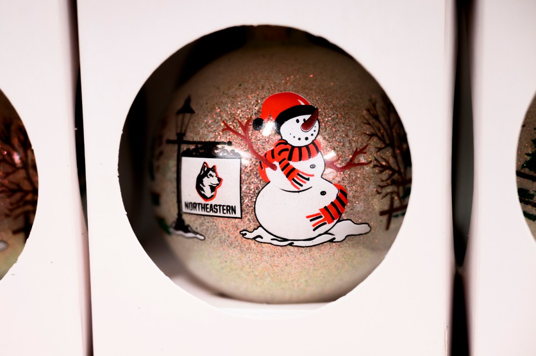 A Christmas ornament with a snowman, the text Northeastern, and a husky. There is glitter inside.