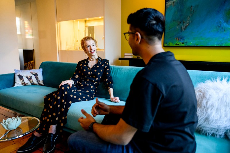 Amy Dabelmont Burnes sitting on a blue couch speaking with Harsh Shah.