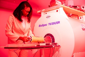 A person wearing a lab coat works with a white machine in a red-lit room.