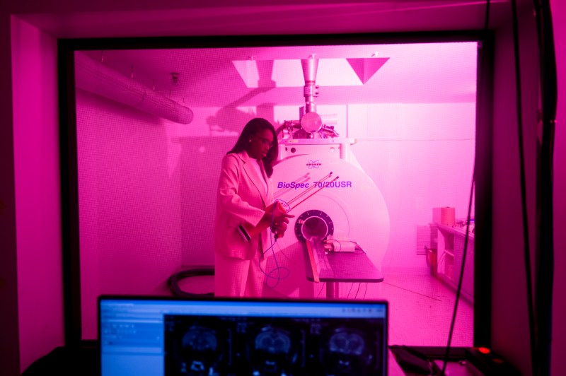 A person wearing a lab coat works in a pink-lit room. 