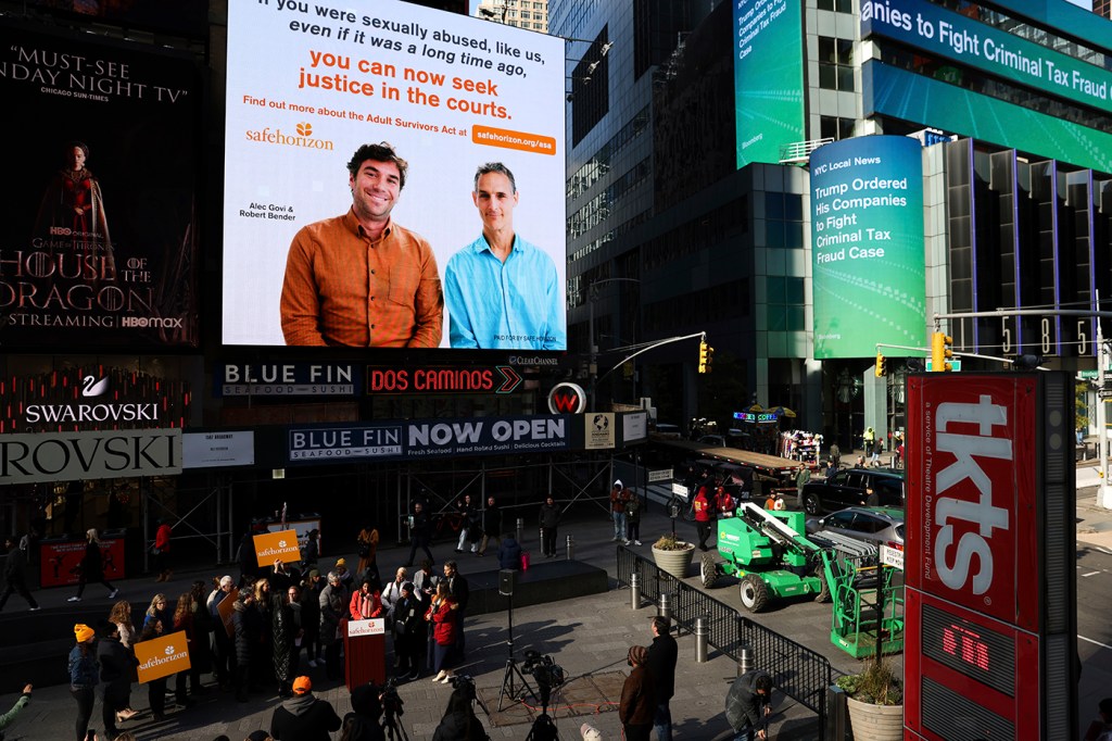 A PSA about the Adult Surivvors act displaying two people and some text playing on a screen in Times Square.