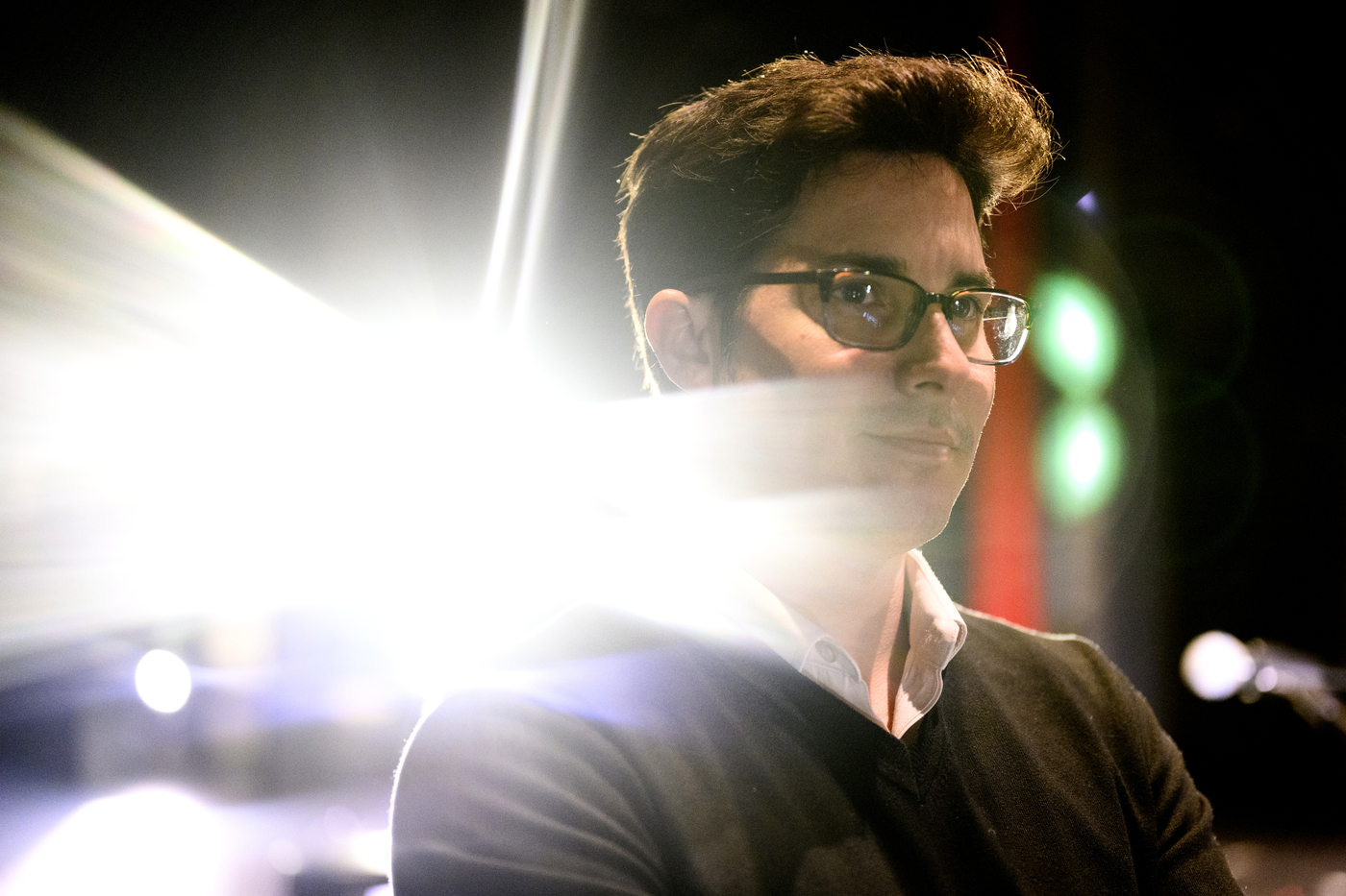 James Gutierrez, an assistant teaching professor of music at Northeastern, stands on a stage with light beaming behind him.
