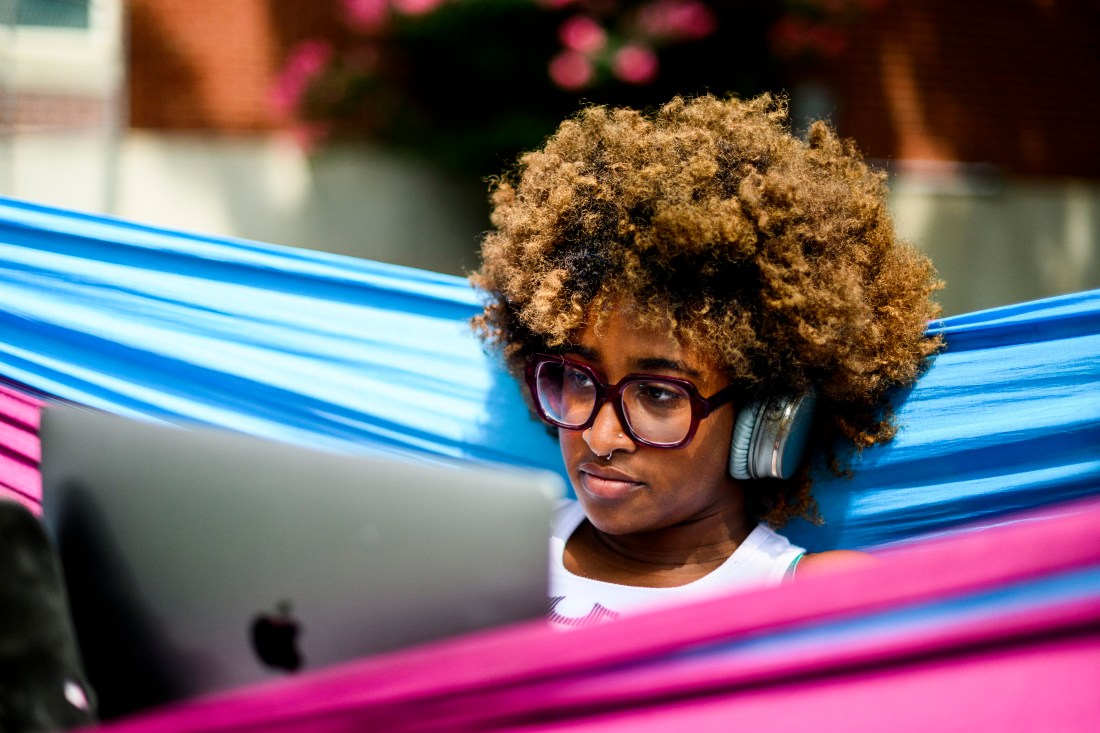 Person wearing headphones while sitting in a hammock working on their laptop.