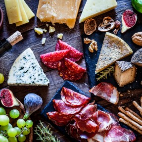 A rustic wooden table topped with cheese, grapes, and cured meats.