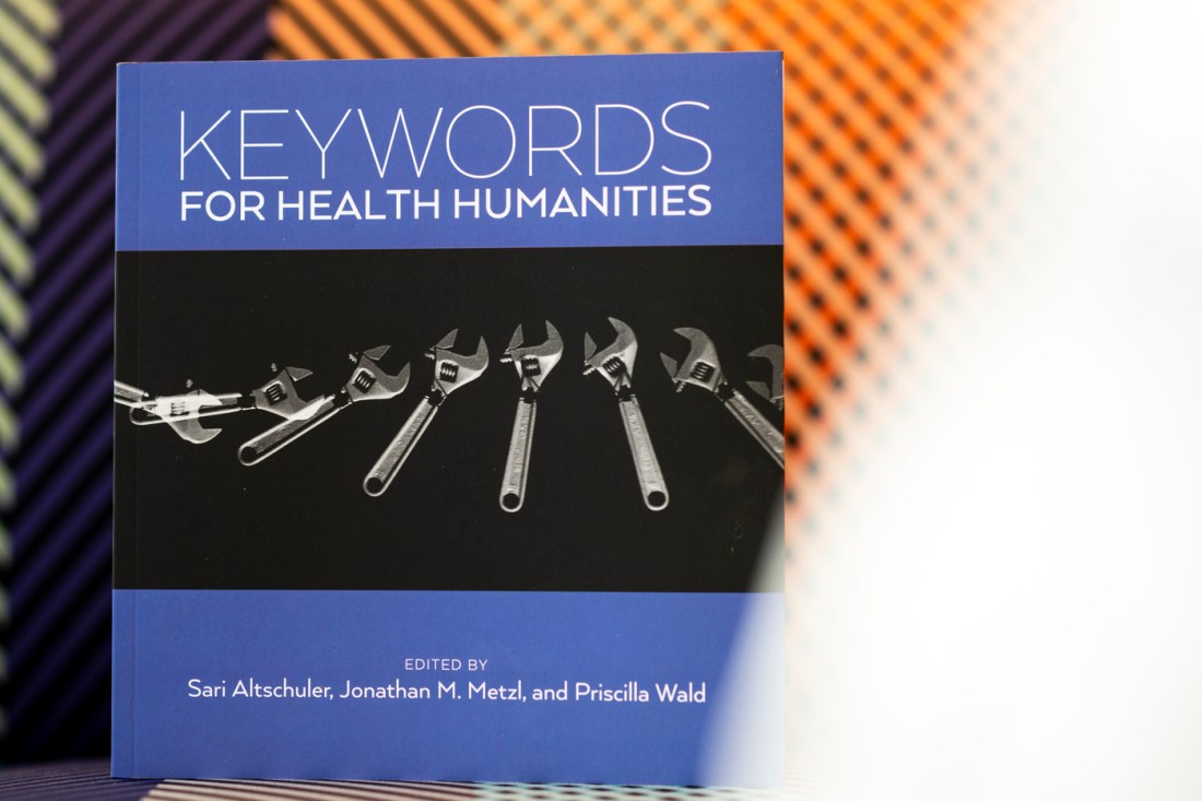 A blue textbook titled "Keywords for Health Humanities" against a dimpled orange background. A photograph of wrenches graces the cover of the book.