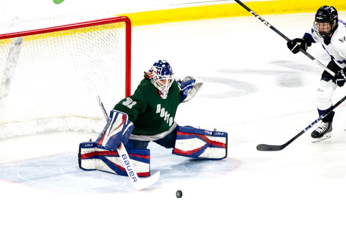 A hockey goalie tries to block a puck from entering the goalpost. 