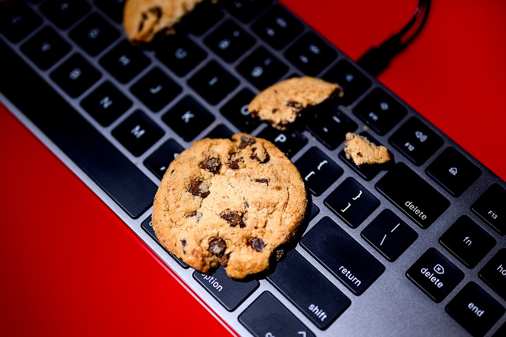 A chocolate chip cookie lays on top of a keyboard on a red-colored surface.