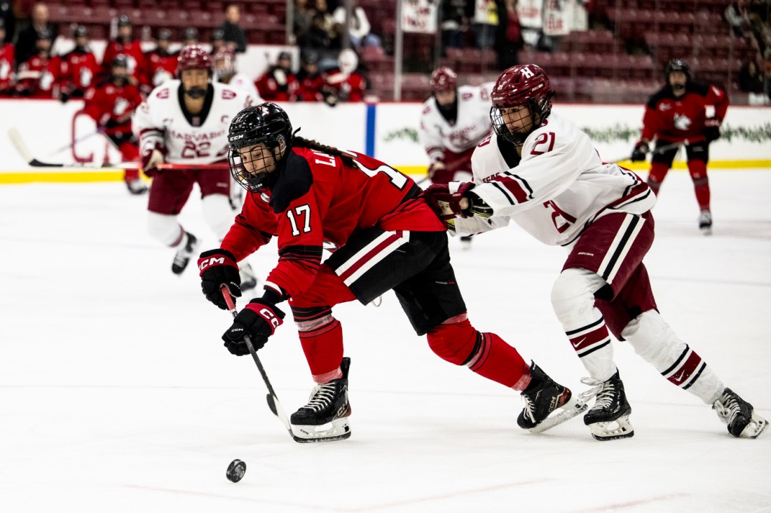 Two hockey players battle it out at the Women's Beanpot Semifinal while players chase after them.