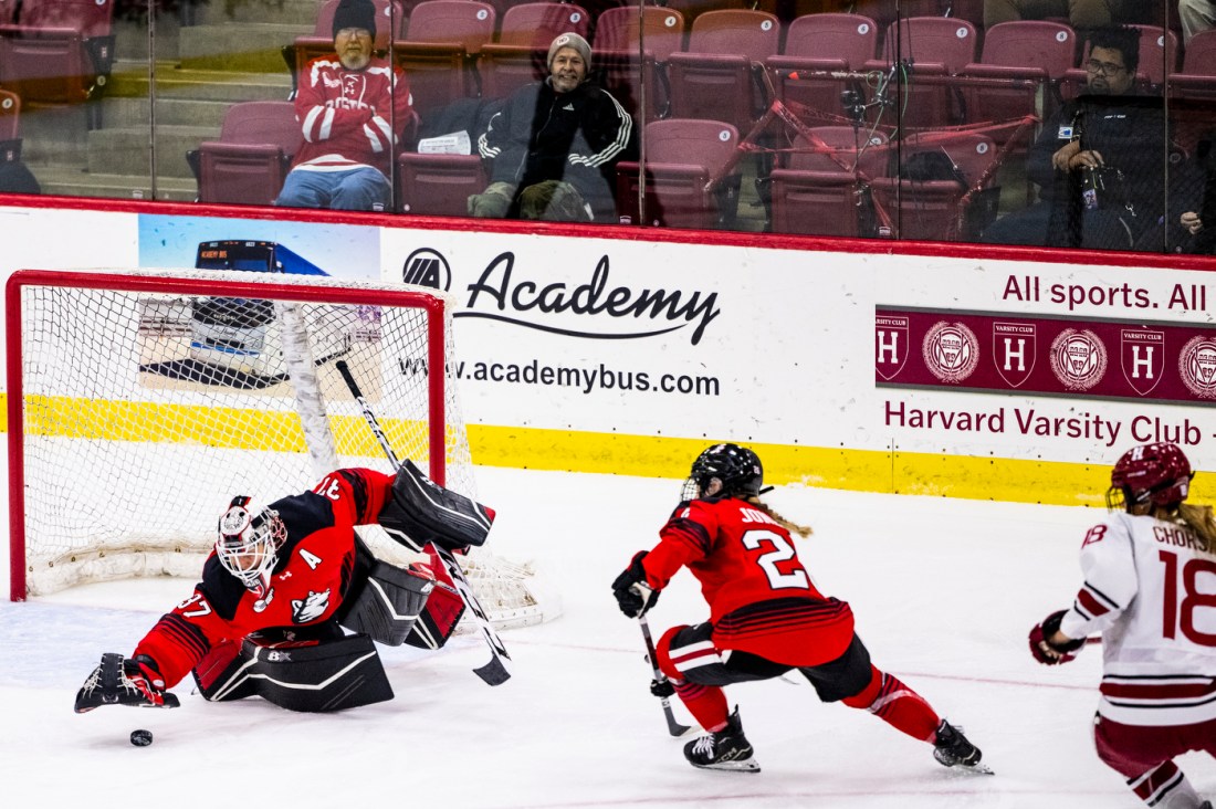 Three hockey players battle it out at the Women's Beanpot Semifinal for a puck on the ice.