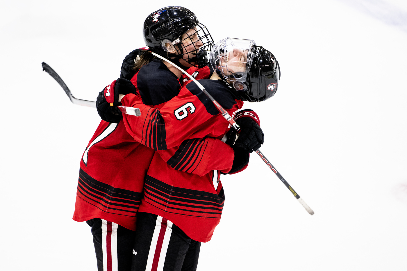 Two Northeastern hockey players hug each other on an ice rink after winning the Women's Beanpot Semifinal at Harvard.