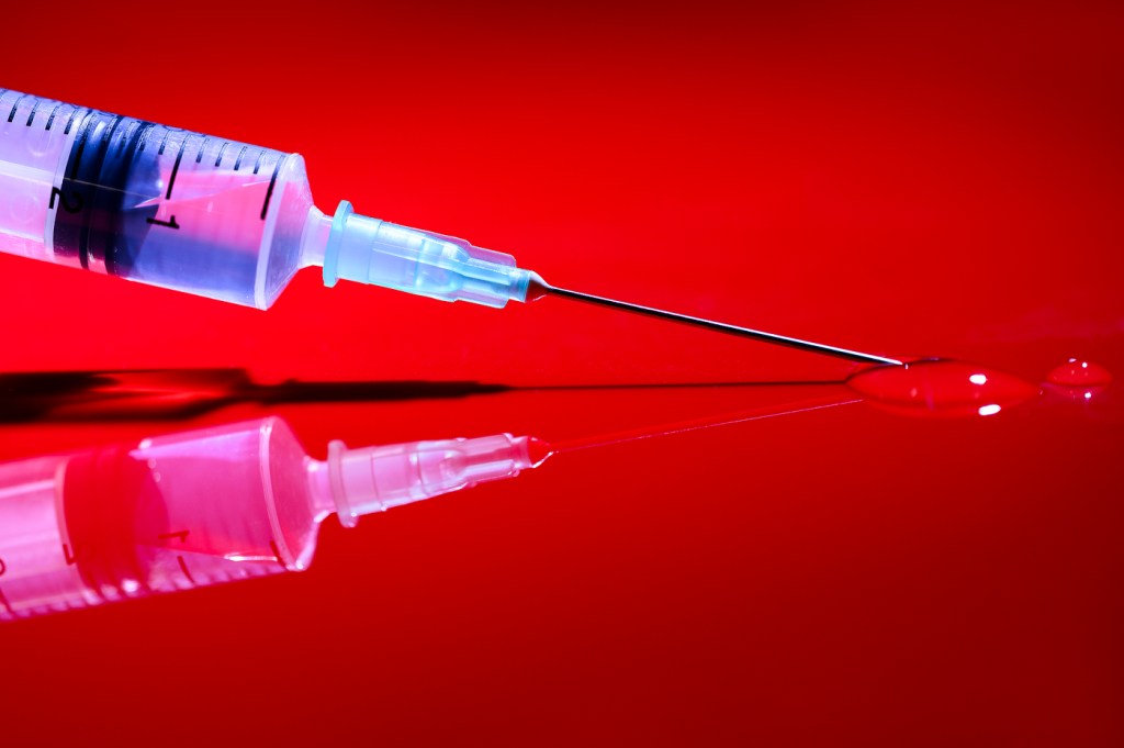 Syringe resting on a red background.