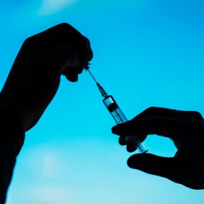 Silhouette of a person's hands filling a vaccine syringe.