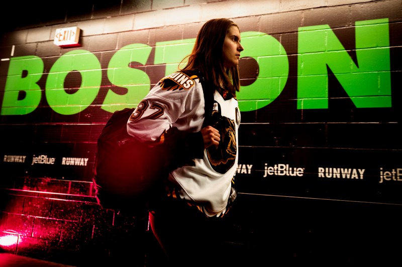 Northeastern women's hockey team member walking in front of a wall that says 'Boston' on it in green letters.