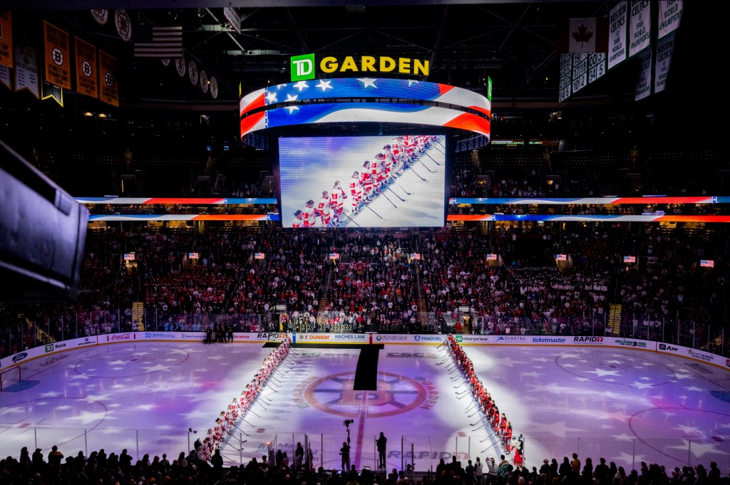 The jumbotron hangs above the ice with players from BU lined up in a row on the left and players from Northeastern lined up in a row on the right.