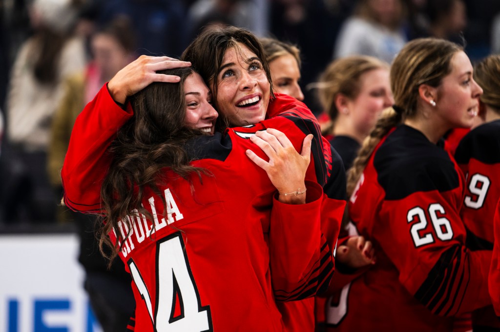 Two members of the Northeastern women's hockey team hug on the ice.