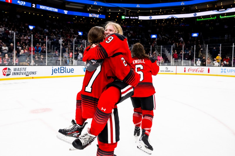 Two Northeastern women's hockey team members hugging each other.