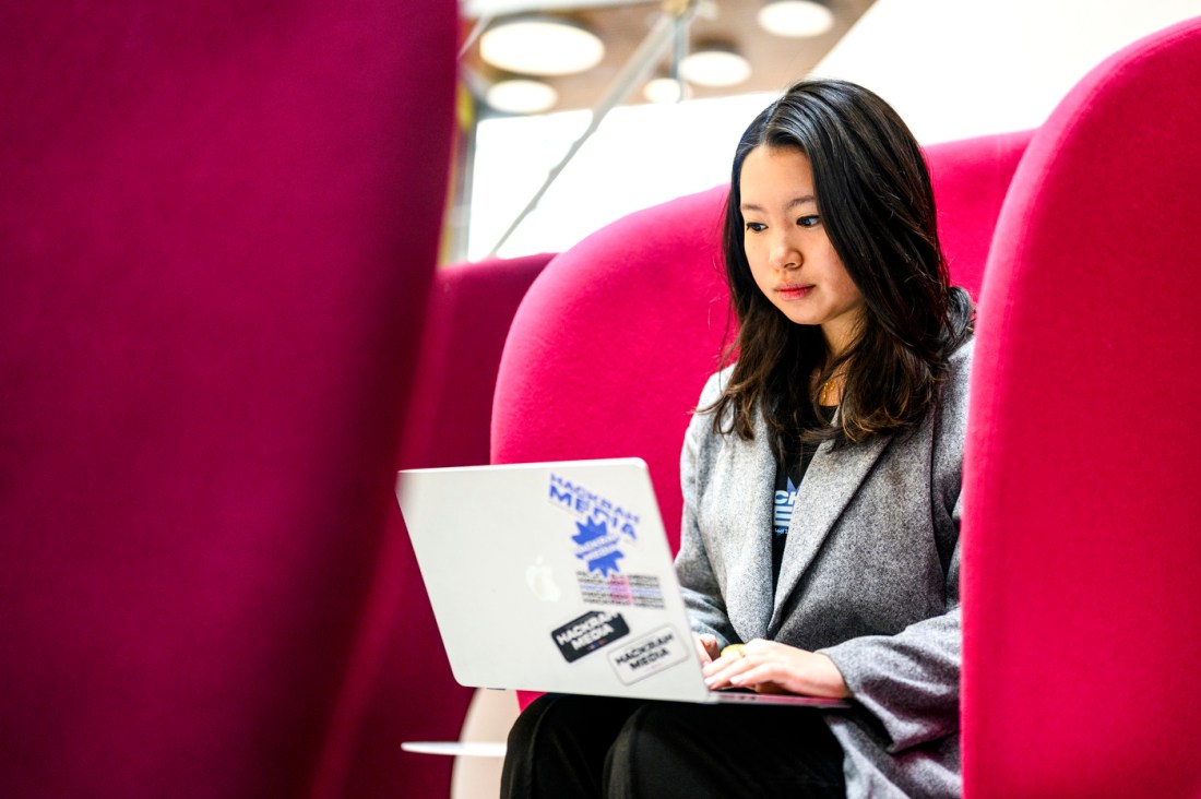 Shirley Wang sitting in a pink chair in ISEC working on her laptop.