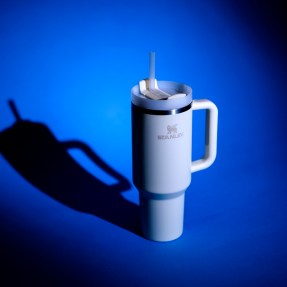 A white stanley cup on a blue background lit up by studio photo lights.