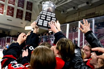 Northeastern's women's hockey team holds a trophy together in a circle while cheering.
