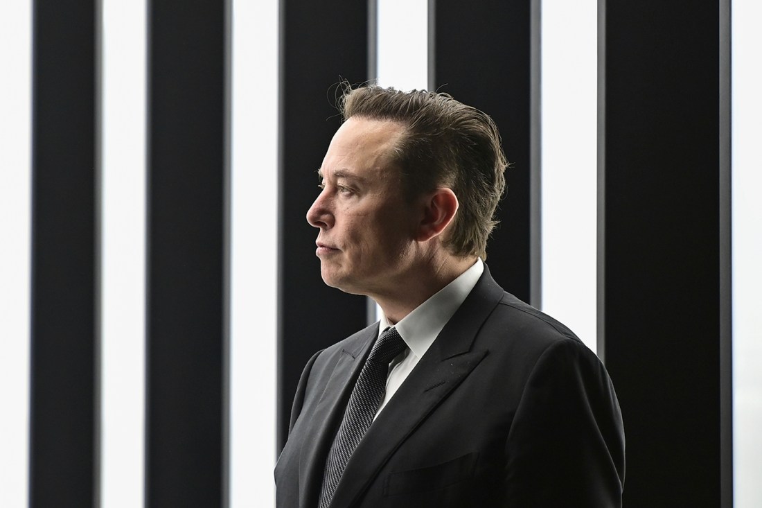 Elon Musk in front of a back and white vertically striped background at the opening of a Tesla factory.