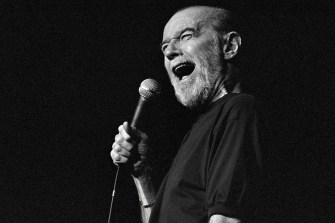 George Carlin holding a microphone while performing standup.