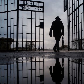 Silhouette of a man walking through the gate of a Nazi death camp in Germany.