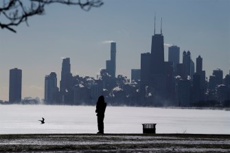 Silhouette of a woman bundled up standing in the cold in front of Lake Michigan in Chicago.