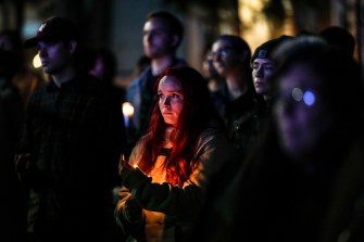 A person in a crowd holds a candle at a vigil at night.