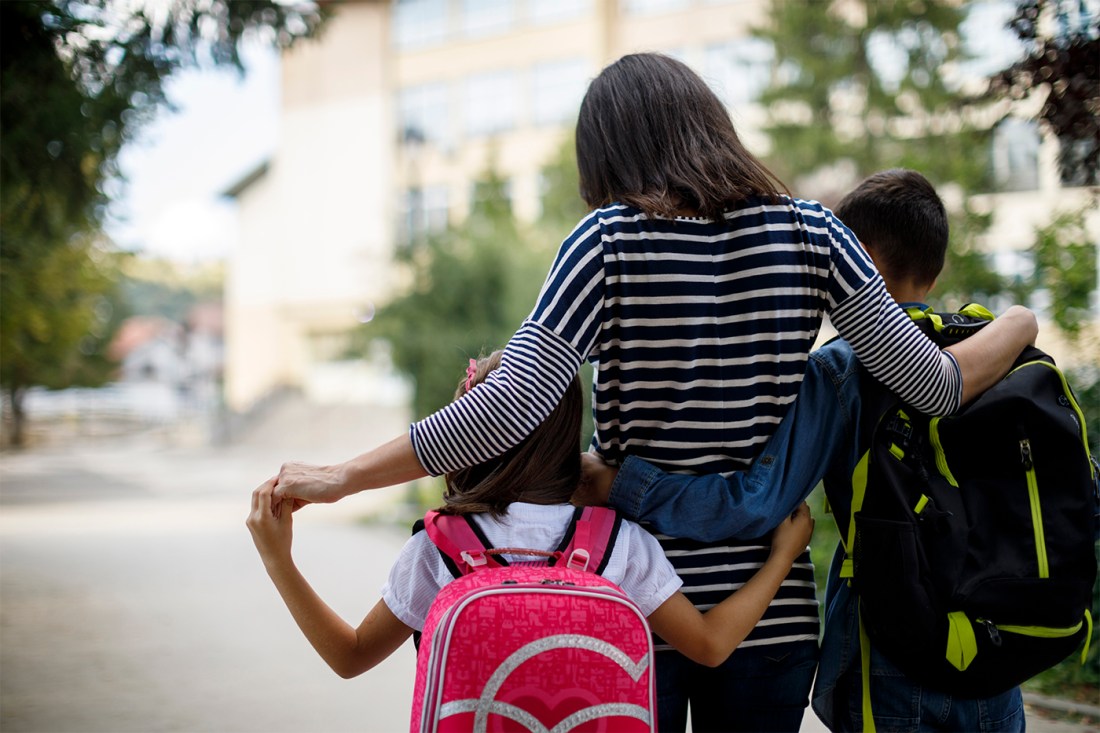 A person walks in the middle of two kids outside on a sunny day.