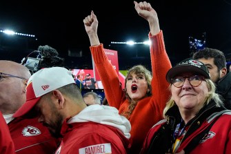 Taylor Swift cheering with her arms up while standing next to Donna Kelce watching the Kansas City Chiefs receive a trophy.