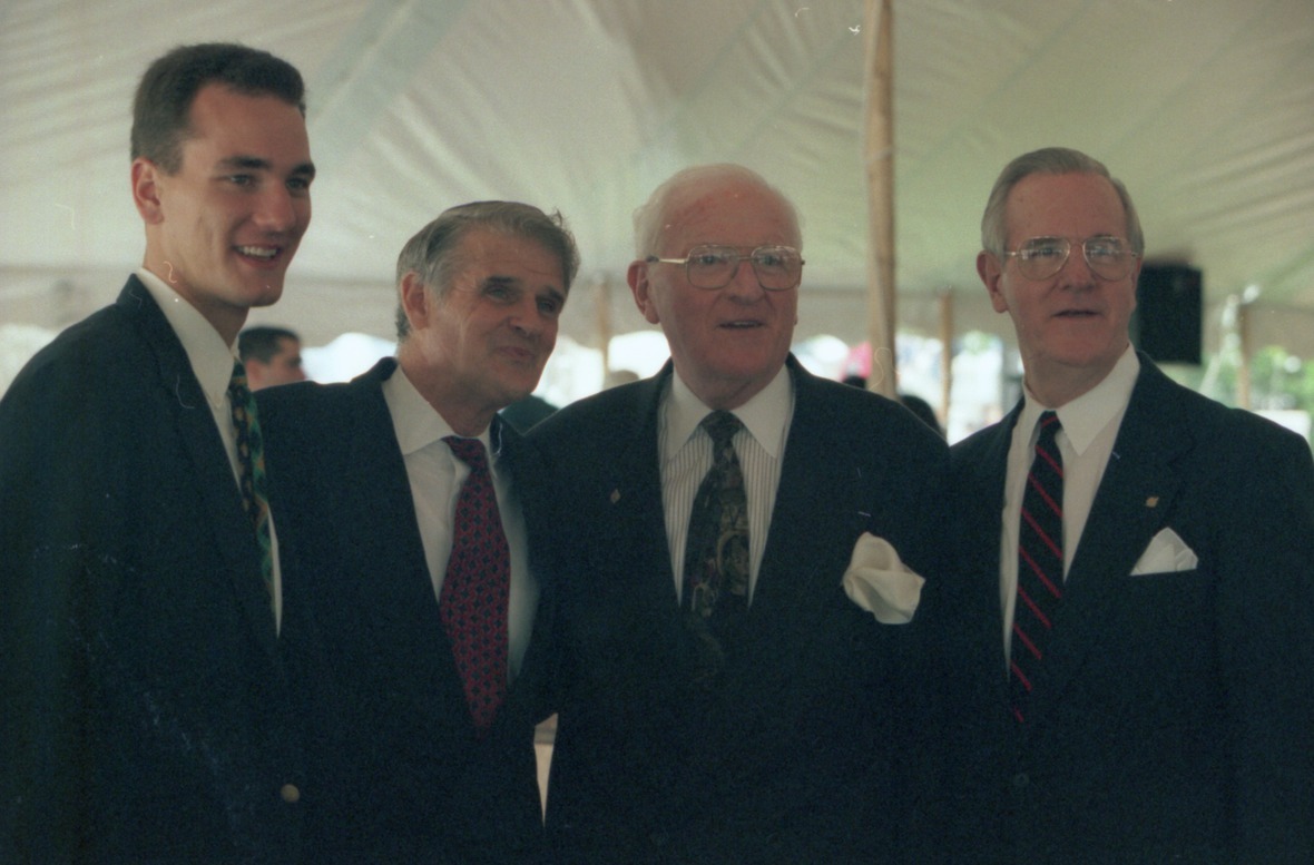 Four people in suits, including George Matthews, pose in a white tent for a picture.