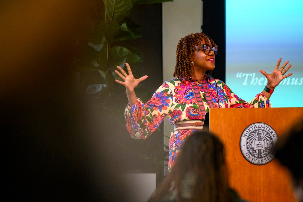 A person wearing a multi-colored shirt speaks to an audience at the annual bell hooks symposium.