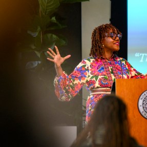 A person wearing a multi-colored shirt speaks to an audience at the annual bell hooks symposium.