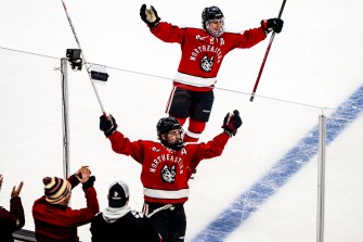 Two Huskies hockey players skating on the ice with their arms up in celebration.