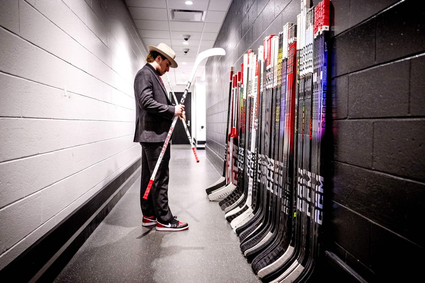 Men's hockey player in a suit and a felt hat holding hockey sticks in the hallway in TD Garden.