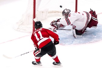 A hockey player spikes a punch into a goal while a goalie tries to block the punch from going in before it ultimately does.