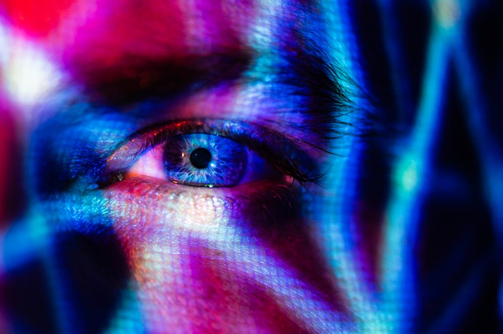 Purple, pink, and blue light shine brightly on a human's eye.