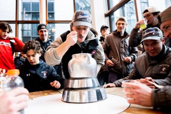 A group of hockey players are sitting around a circular table, munching on cereal from a trophy made of silver-colored metal.