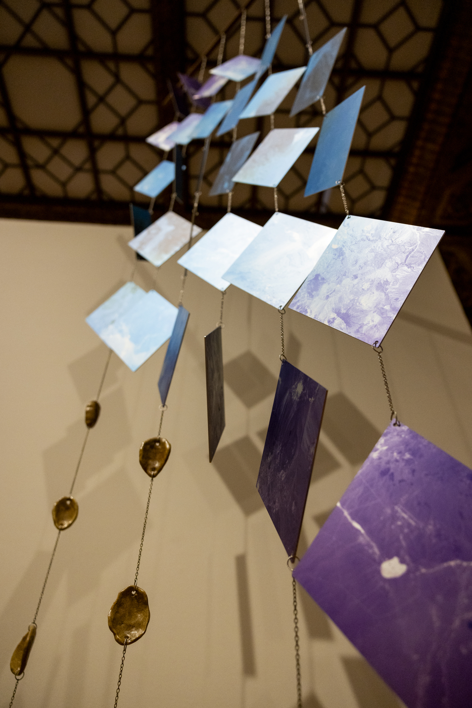 Blue and purple triangles and teardrop-shaped gems strung on wire up to the ceiling of an art gallery.