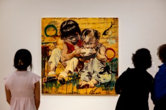 Three people looking at a painting on the wall of an art gallery.