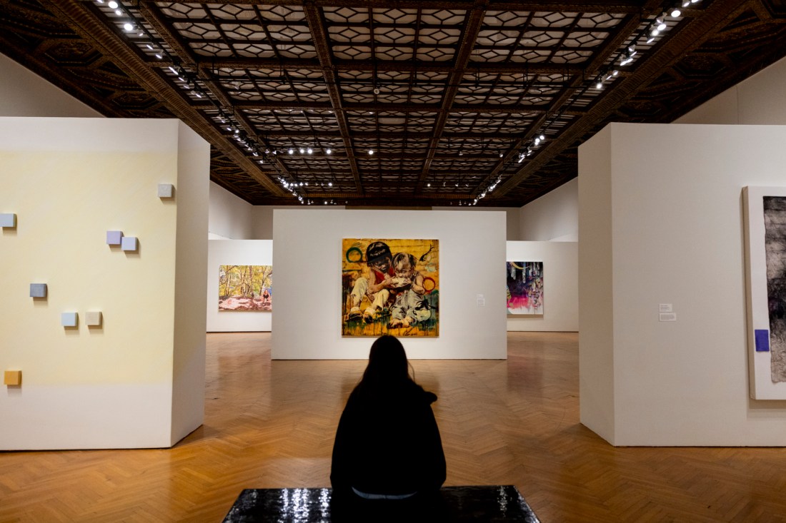A person standing in the room of an art gallery with several walls displaying paintings.
