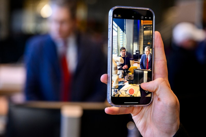 Someone holds a smartphone to take a picture of two people in an office setting.