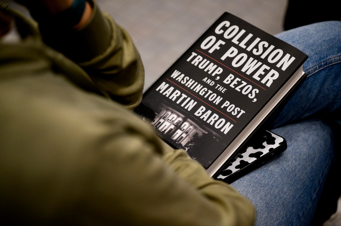 A person sitting with a copy of Marty Baron's book 'Collision of Power' in their lap.