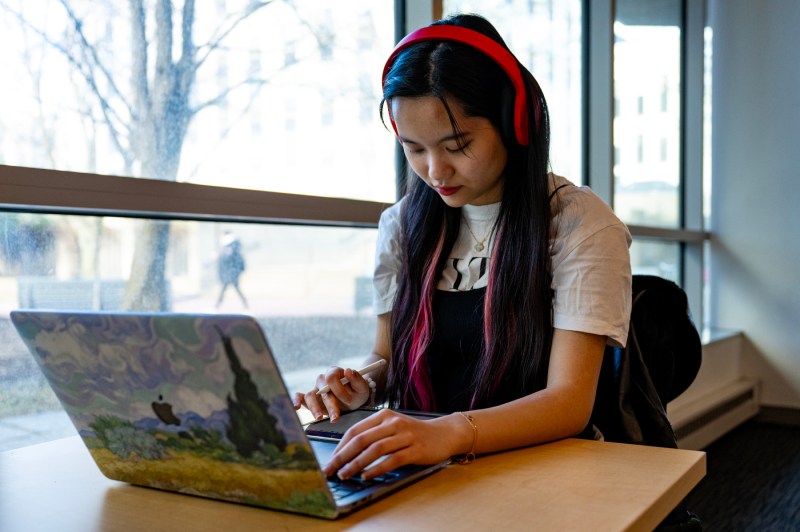 A person wearing red headphones works on a laptop near windows.