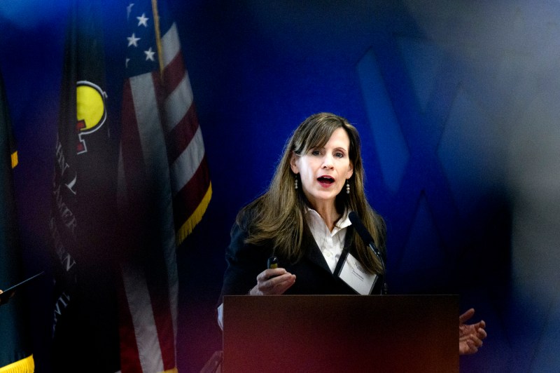 Alicia Modestino speaks at a podium in front of a blue background.