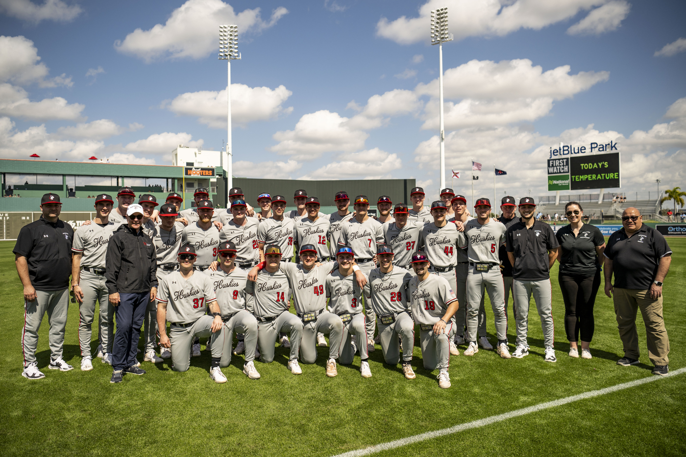 Northeastern men's baseball team poses for a picture on a field outside before facing off against the Boston Red Sox.