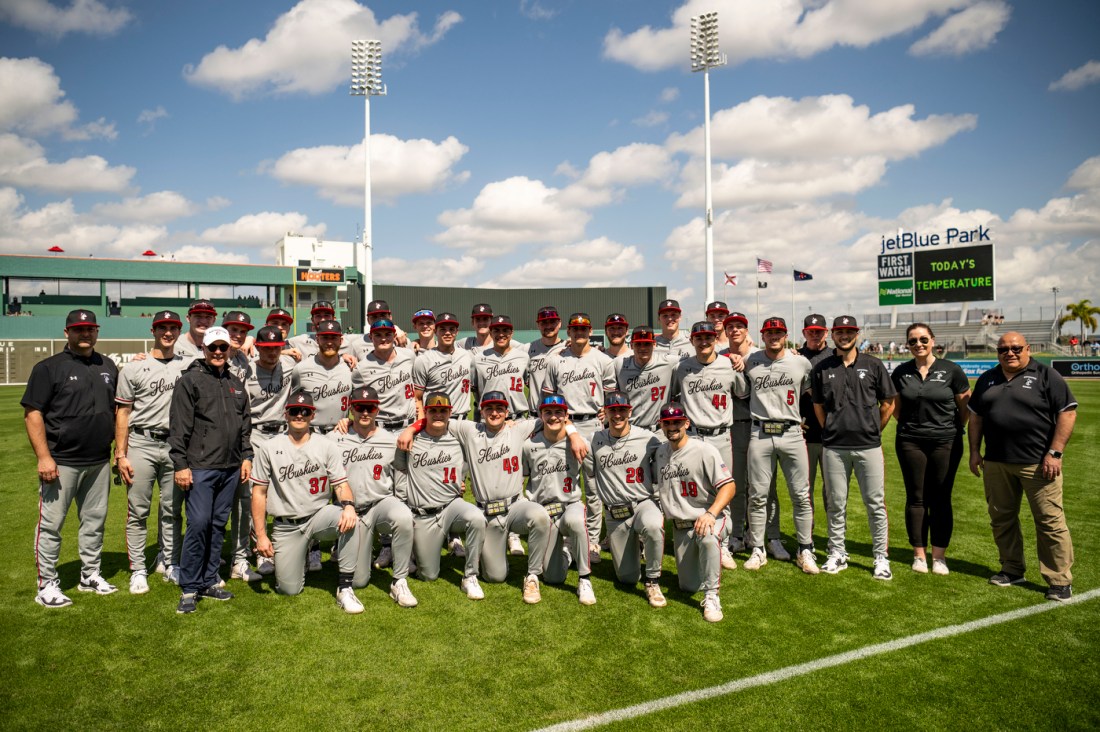 Northeastern men's baseball team poses for a picture on a field outside before facing off against the Boston Red Sox.